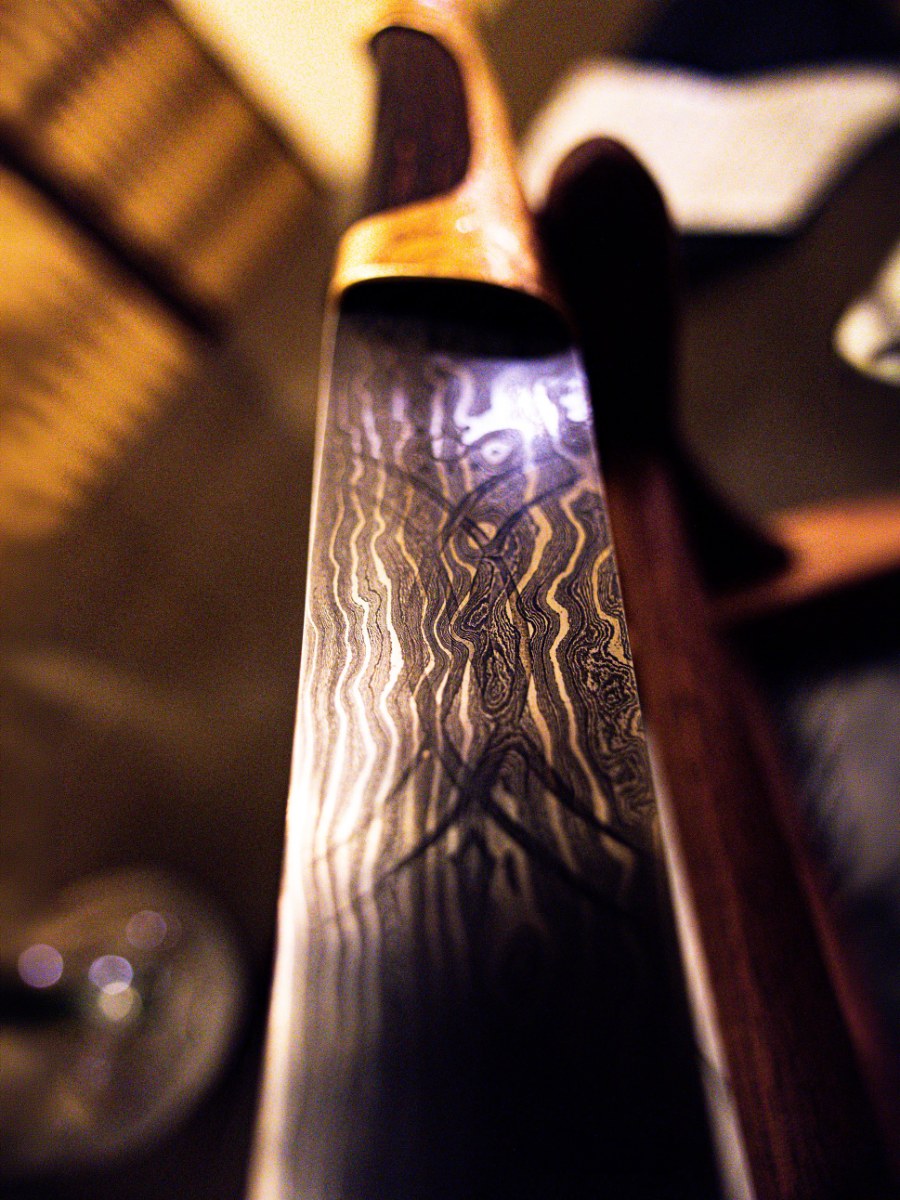 A Damascus steel crysknife, its folded pattern visible along the blade