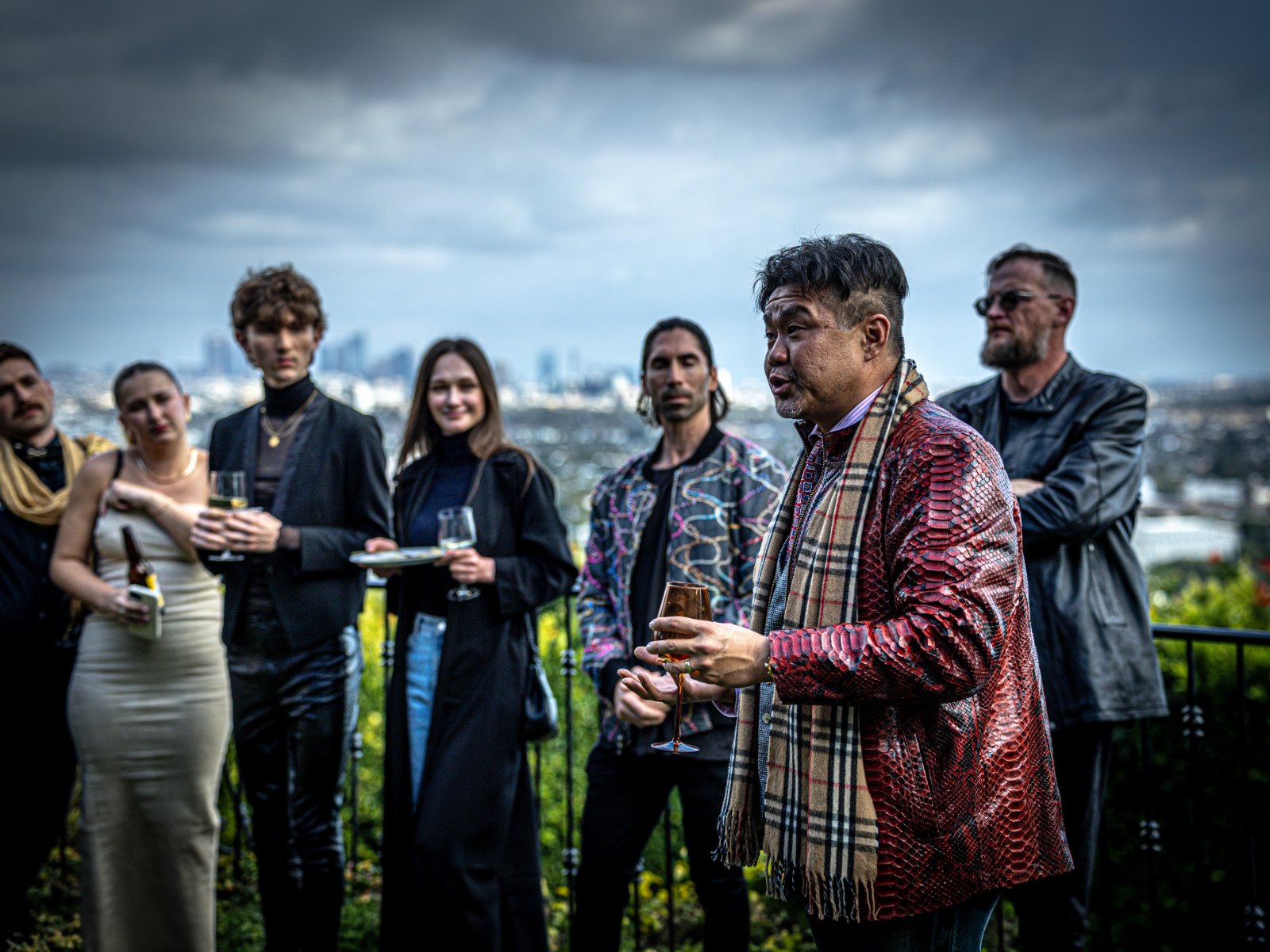 Guests with drinks on a terrace above the city, listening to the host